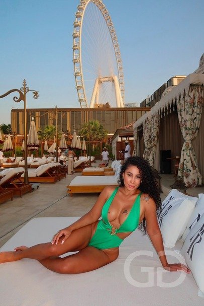 Nicole in a green swimsuit lounging on a white daybed at a beach club