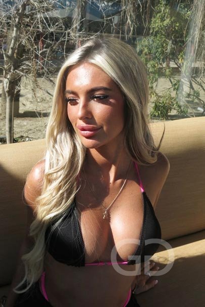 Alana, Essex blonde escort, in a black and pink bikini in the sun